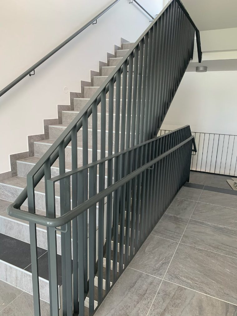 Stiegenhaus mit grauem Stabgeländer und Handlauf