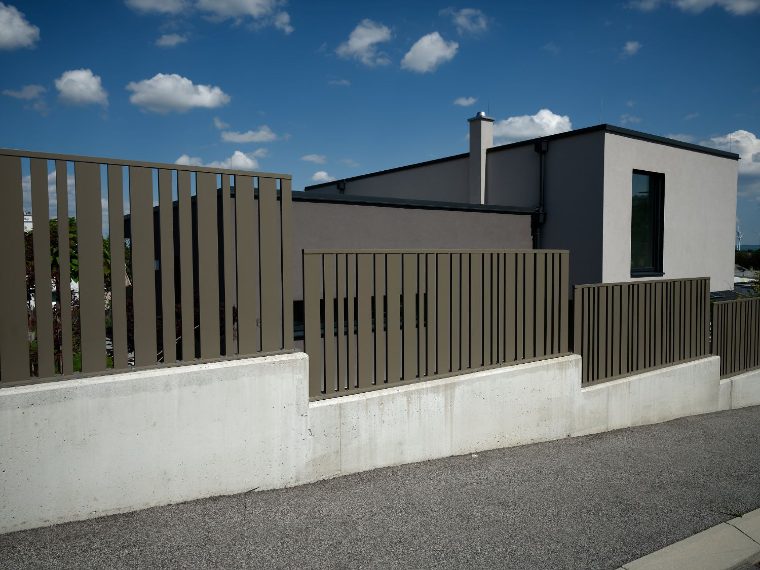 Moderner Lattenzaun aus Metall auf einem Betonsockel vor einem Neubau